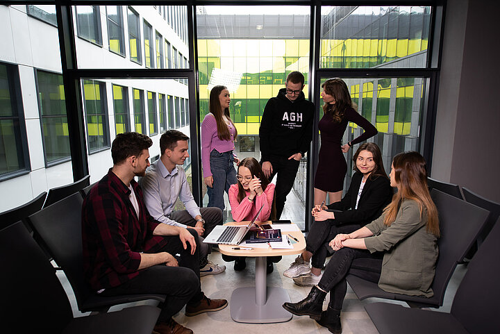 Grupa studentów Wydziału Humanistycznym wspólnie pracuje przy stoliku w nowoczesnym przeszklonym wnętrzu uczelni.